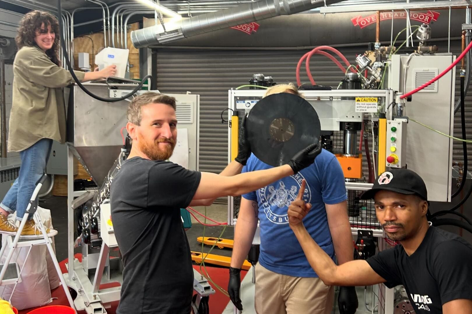 Hellbender Vinyl employees pose with a vinyl record in the Pittsburgh pressing plant