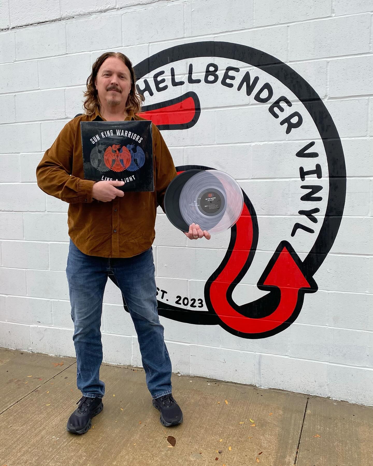 Jim Donovan holding black and clear vinyl 12" variants of the Sun King Warriors album in front of Hellbender Vinyl