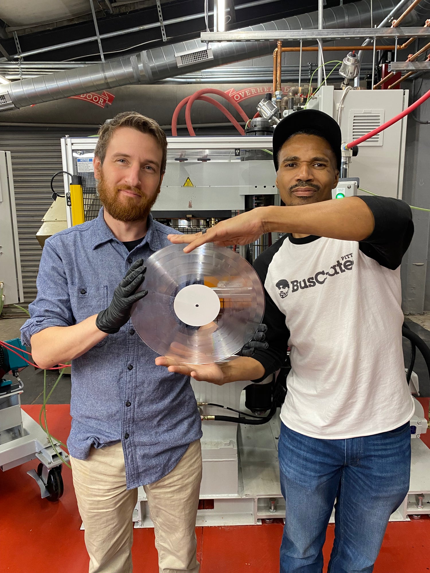 Hellbender Vinyl employees Nick and Orlando pose after inspecting a clear vinyl record for quality control