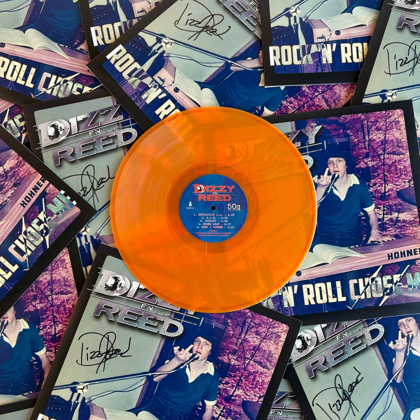 Hazy orange vinyl record with a blue label on top of Dizzy Reed album covers