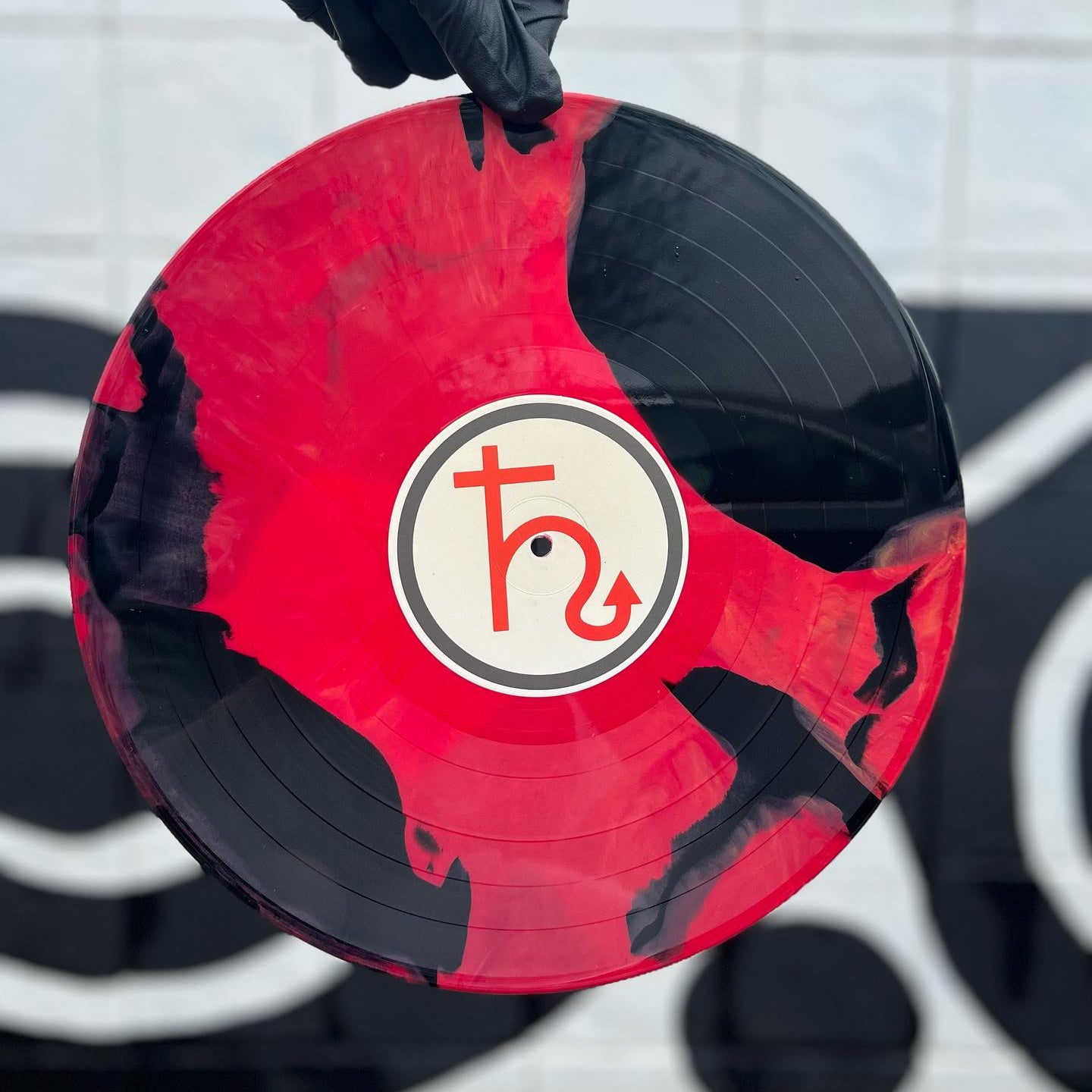 Red and black vinyl record with a logo held by a gloved hand against a blurred background