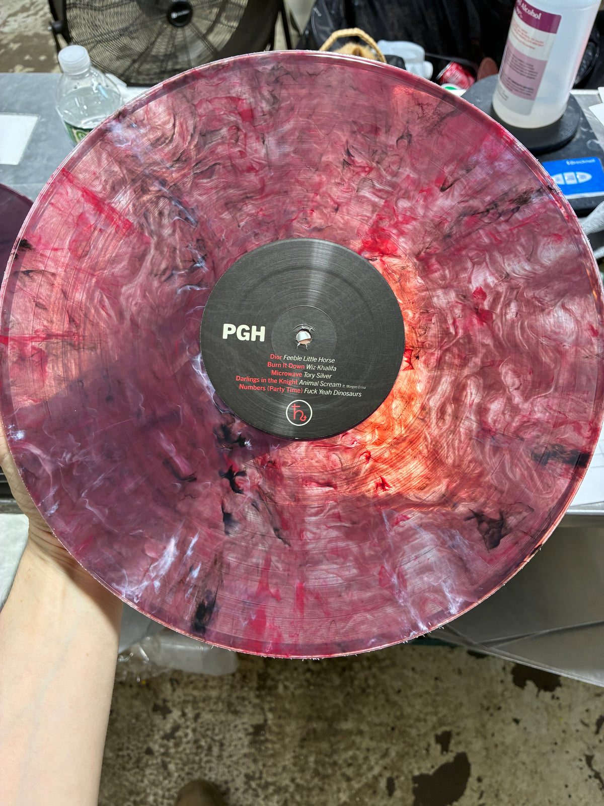 A marbled vinyl record with a red, pink, and purple swirl pattern, held up by a hand. 