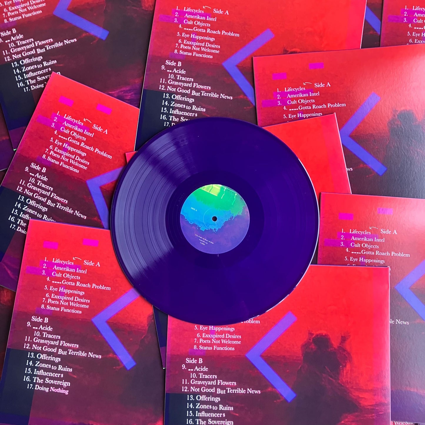 Purple vinyl record with colorful label surrounded by red album covers with text