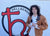 Person holding a stuffed dog toy in front of a 'Hellbender' logo on a wall.