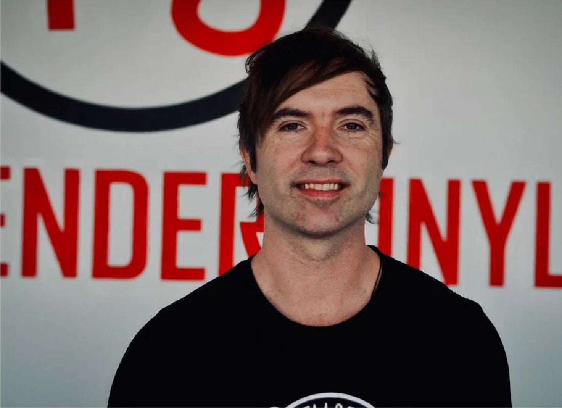 Man wearing a black shirt in front of a red and white background with text